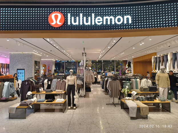 Das Innere eines lululemon-Ladens in Singapur mit Schaufensterpuppen in der neuesten Mode, Kleidung an Bügeln, Tischen mit verschiedenen Artikeln, Deckenleuchten, einem Namenbrett mit Text und einem Wasserzeichen auf dem Bild.