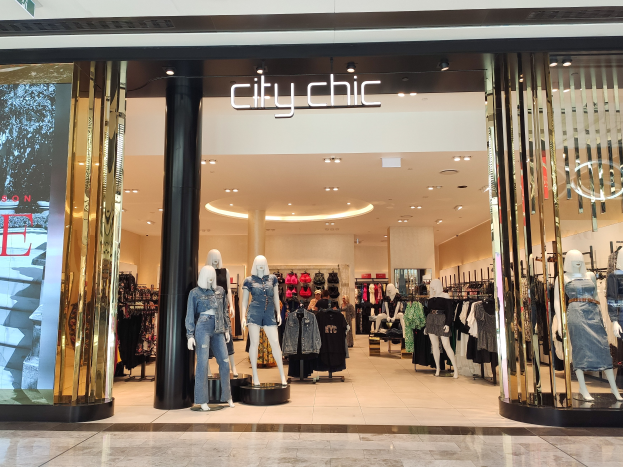 Ein stylischer Mode-Laden in einem Einkaufszentrum mit Schaufensterpuppen in der neuesten Mode, Kleidung an Bügeln, einer Säule, einem Schild, Deckenlampen und einem Fliesenboden.