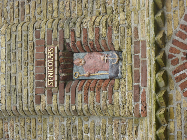 Eine Backsteinmauer mit einer Steinplatte, auf der in fetter Schrift 'St. Nikolaus' steht.