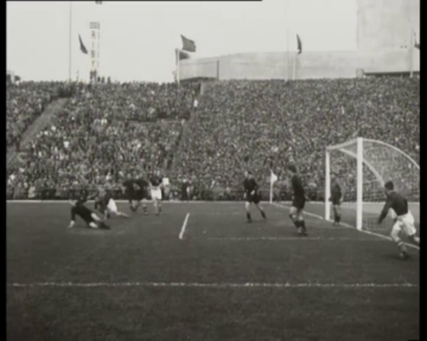 Ein Schwarz-Weiß-Foto von einem WM-Finale 1958 zwischen Manchester United und Liverpool mit Spielern auf dem Feld und Zuschauern auf den Rängen bei klarem Himmel.