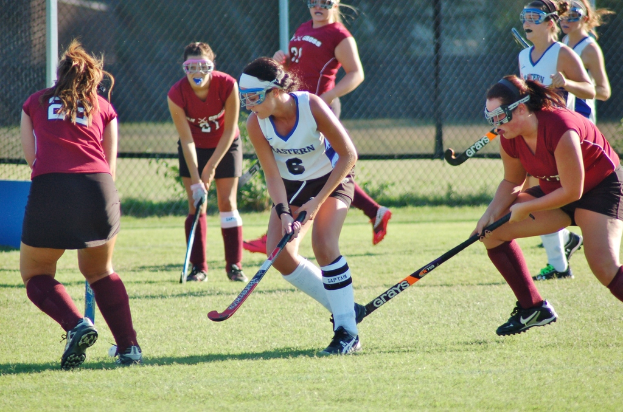 Frauen spielen Hockey auf einem Rasenfeld mit einem Netz im Hintergrund.