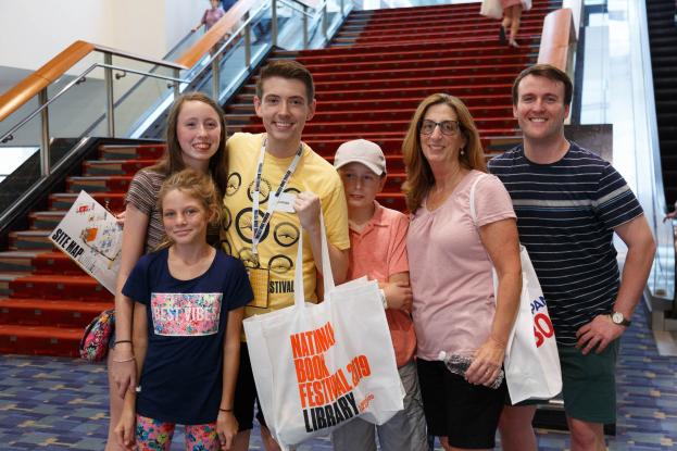 Gruppe von Menschen, die vor einer Rolltreppe an der Nationalen Buchmesse 2019 lächeln und Taschen halten.