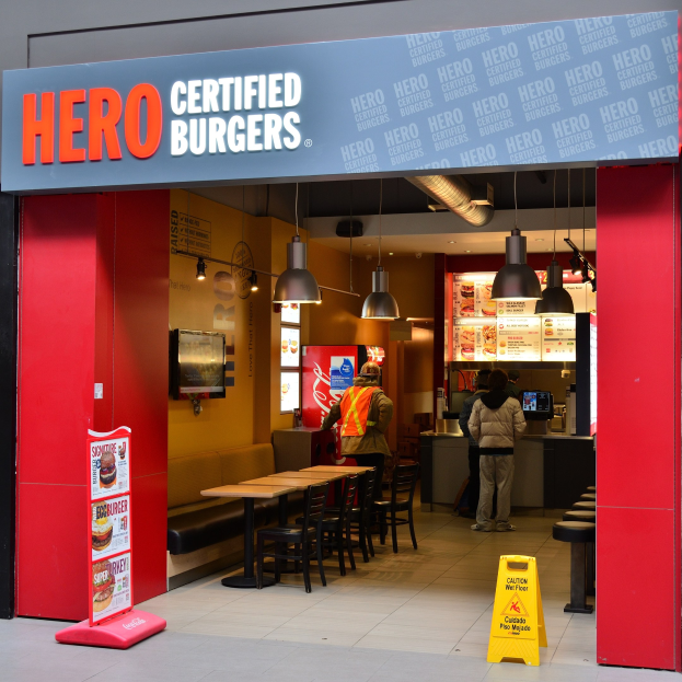 Außenansicht eines Hero Certified Burgers Restaurants in London, England, mit Gästen, Sitzgelegenheiten, einer Speisekarte, einem Wandfernseher und Deckenleuchten.