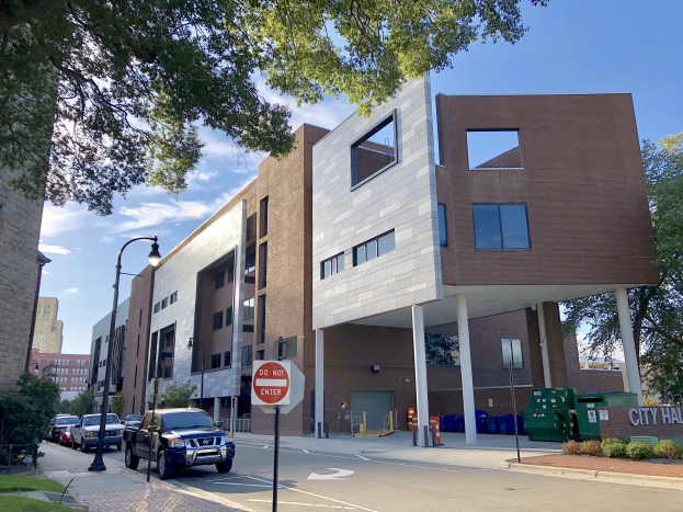 Großes Gebäude mit zahlreichen Fenstern, beschriftet mit "Stadthallen Apartments", umgeben von Straßeninfrastruktur, Fahrzeugen, Vegetation und einem bewölkten Himmel.