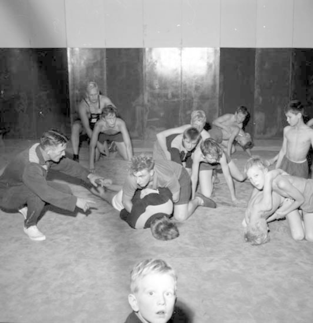 Schwarz-weißes Bild von jungen Jungs, die in einem Fitnessstudio ringen, mit einer Wand im Hintergrund.