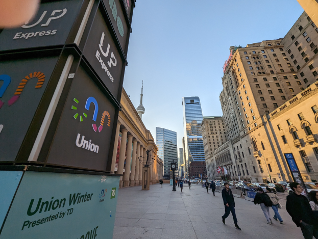 Eine belebte Stadtstraße mit Fußgängern, hohen Gebäuden, Fahrzeugen und Texttafeln im Hintergrund, die sich auf die Union Winter Conference beziehen.