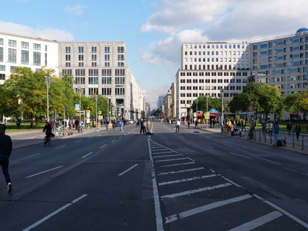 Eine belebte Stadtstraße in Berlin, Deutschland, mit Fußgängern und Radfahrern, die die Straße mit hohen Gebäuden, Bäumen, Laternen und Schildern teilen.