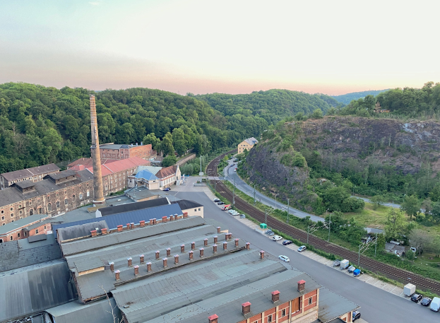 Luftaufnahme einer Stadt mit dichtem Gebäudebestand, befahrenen Straßen, Strommasten, verstreuten Bäumen, fernen Hügeln und einem bewölkten Himmel, was auf ein Kohlerevier hindeutet.