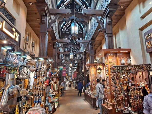 Ein belebter Dubai-Basar mit Menschen, die zwischen Regalen mit Waren hindurchgehen, Wänden mit Text und einer Decke mit warmem Licht.