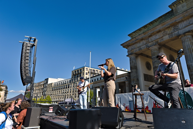 Eine Gruppe von Menschen, die auf einer Bühne Musik spielen, mit dem Brandenburger Tor im Hintergrund.