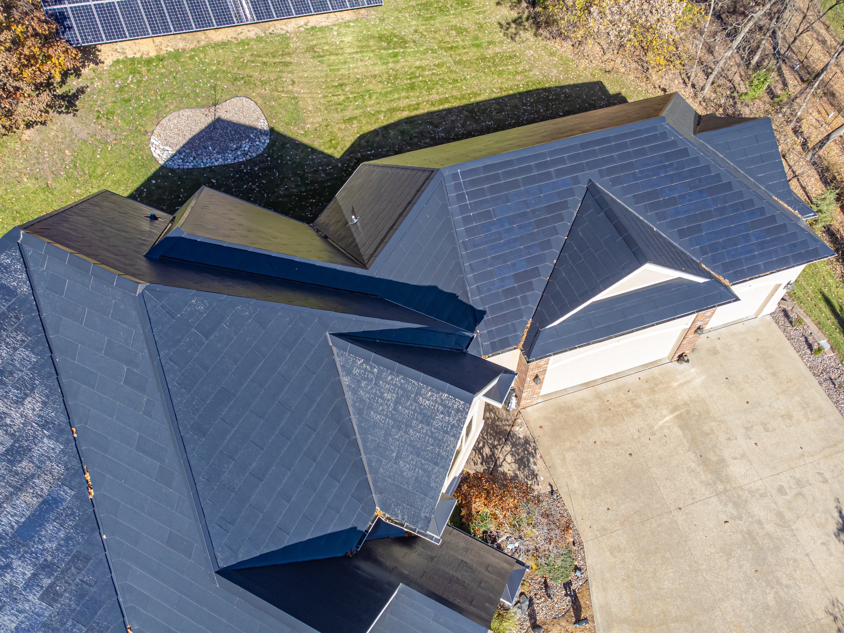 Luftaufnahme eines Hauses mit integrierten Solarpanelen auf dem Dach, umgeben von Bäumen, Gras und einem Zaun.