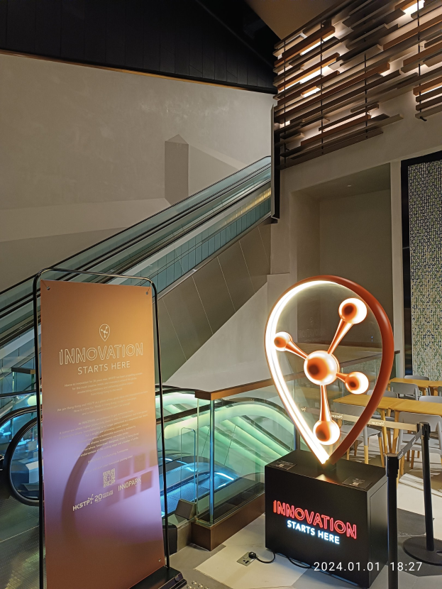 Großes Schild in einem Gebäude mit der Aufschrift "Innovation beginnt hier" und einer Rolltreppe im Hintergrund, Tische und Stühle auf der rechten Seite und ein Expo-Schild für HSTP20 auf der linken Seite.