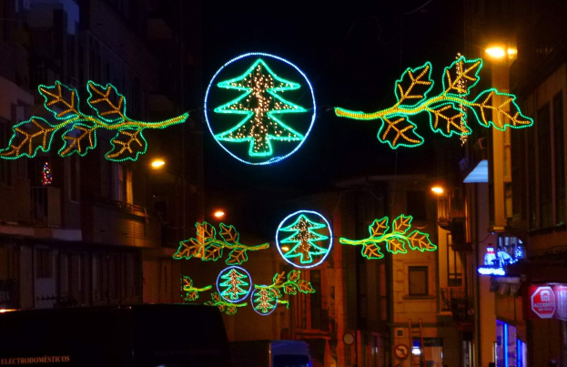 Eine nächtliche Stadtstraße, die mit festlichen Weihnachtslichtern in Form von Blättern geschmückt ist, mit Fahrzeugen auf der Straße und Gebäuden auf beiden Seiten.