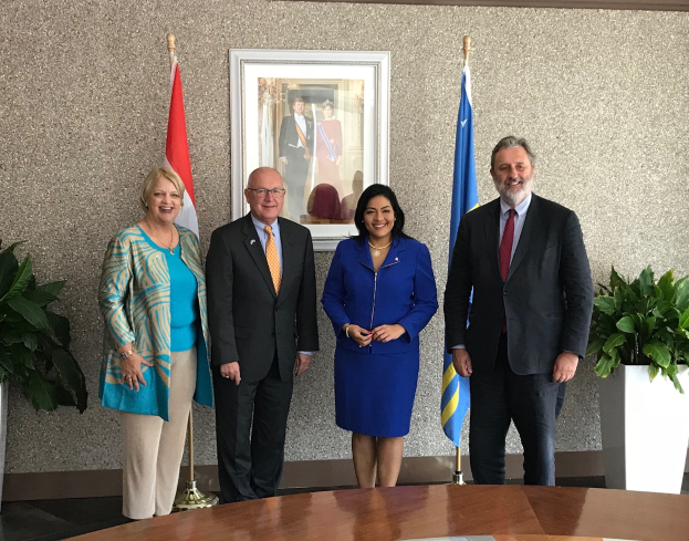 Eine Gruppe strahlender Menschen um einen Tisch mit Papieren stehend, umgeben von Flaggen, Topfpflanzen und einem Fotorahmen an der Wand, feiert die Unterzeichnung eines Memorandums zwischen den Vereinigten Staaten und Kanada.