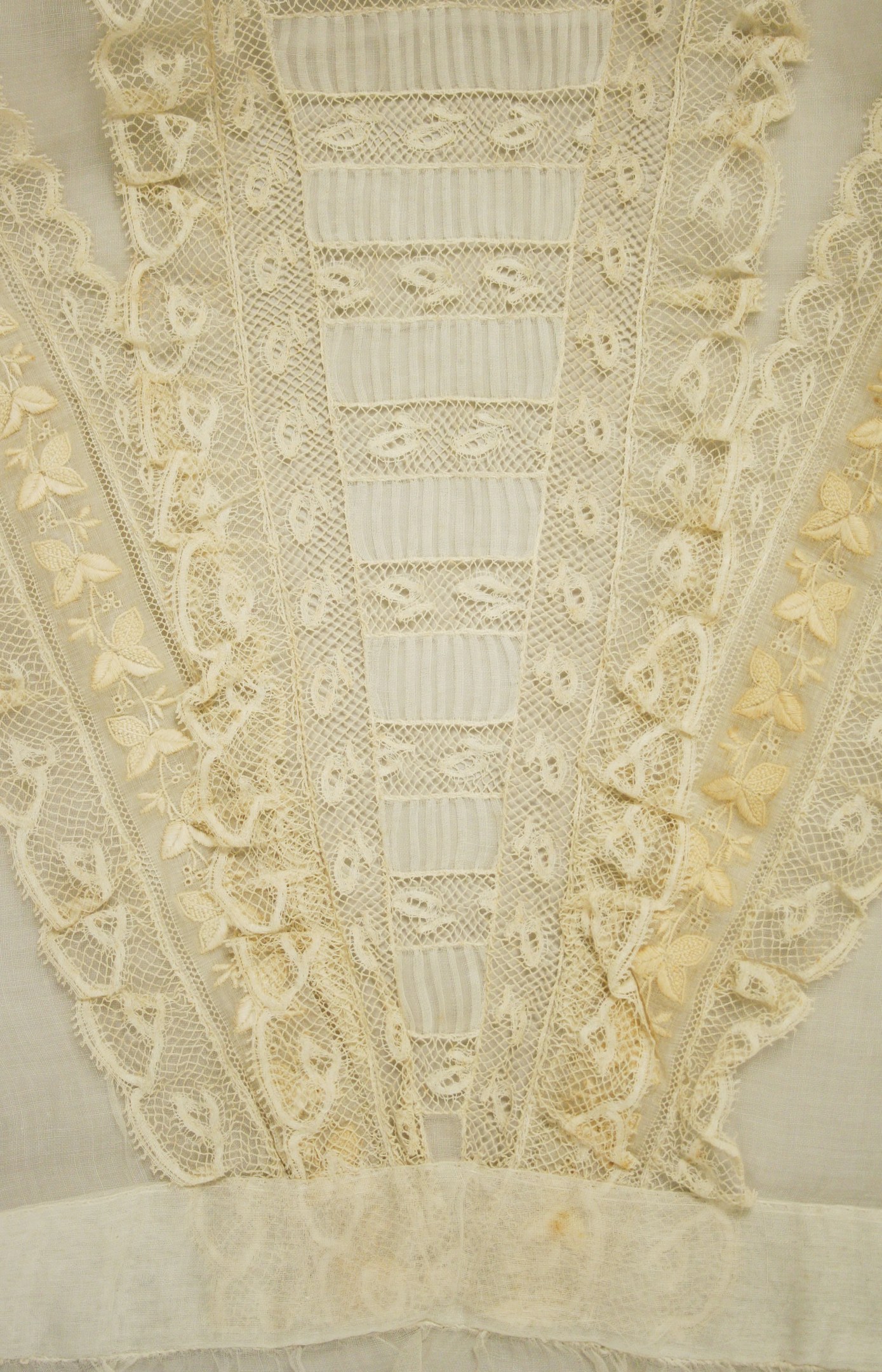 Nahaufnahme eines weißen Kleides mit zarten, detailreichen Spitzenverzierungen in verschiedenen Mustern und Formen, aus leichtem, luftigem Stoff für den Sommer geeignet.