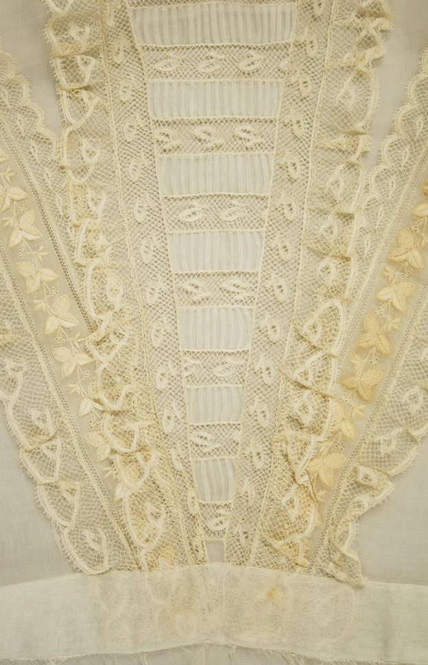 Nahaufnahme eines weißen Kleides mit zarten, detailreichen Spitzenverzierungen in verschiedenen Mustern und Formen, aus leichtem, luftigem Stoff für den Sommer geeignet.