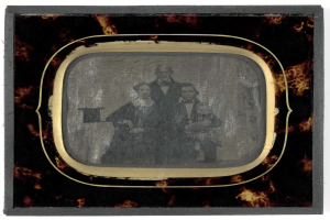 Schwarz-weiß-Foto eines Mannes im Anzug und einer Frau in unbekannter Kleidung vor einem alten Fernseher mit ernsten Gesichtern