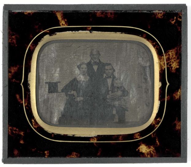 Schwarz-weiß-Foto eines Mannes im Anzug und einer Frau in unbekannter Kleidung vor einem alten Fernseher mit ernsten Gesichtern