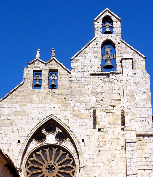 Alte steinerne Kirche mit zwei Glocken oben drauf, umgeben von einem klaren blauen Himmel, geschmückt mit kunstvollen Schnitzereien und Designs, Glocken läuten laut.