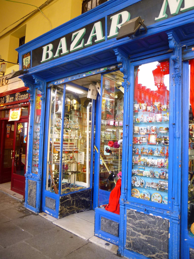 Ein Ladengeschäft mit einer blauen Tür und einem Schild mit der Aufschrift "Bazar", das verschiedene Gegenstände zeigt, die in Schränken angeordnet sind.