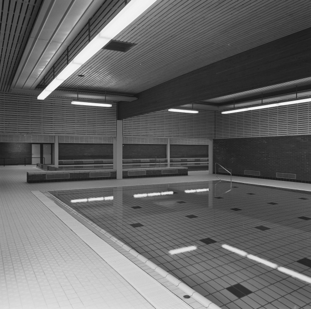 Innenpool mit gefliesten Wänden und Decke, gefüllt mit klarem Wasser, umgeben von ein paar Gegenständen in einem großen, friedlichen Raum.