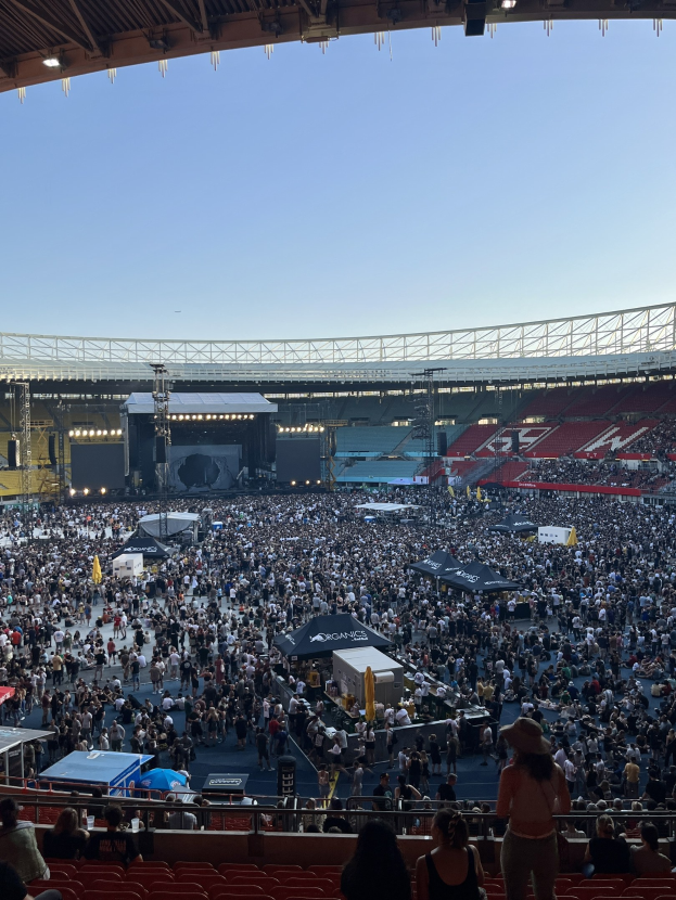 Große Menschenmenge auf Sitzplätzen und Stehplätzen in einem Stadion mit Zelten, Geländern und Deckenbeleuchtung vor einem Himmel als Hintergrund im O2 Arena in London.
