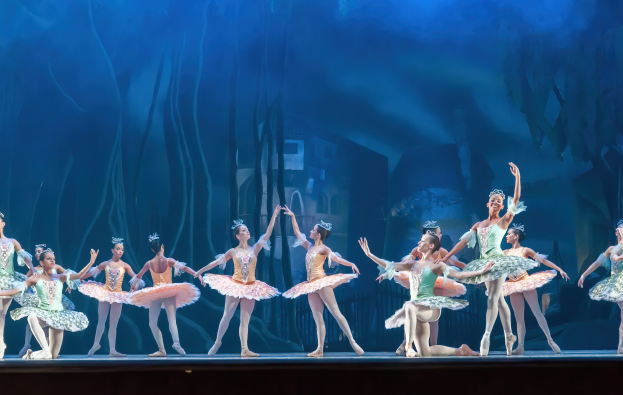 Eine Gruppe von Balletttänzern in bunten Kostümen performs *Der Nussknacker* auf der Bühne der Royal Opera House, sich in synchroner Anmut gegen einen blauen Hintergrund bewegend.
