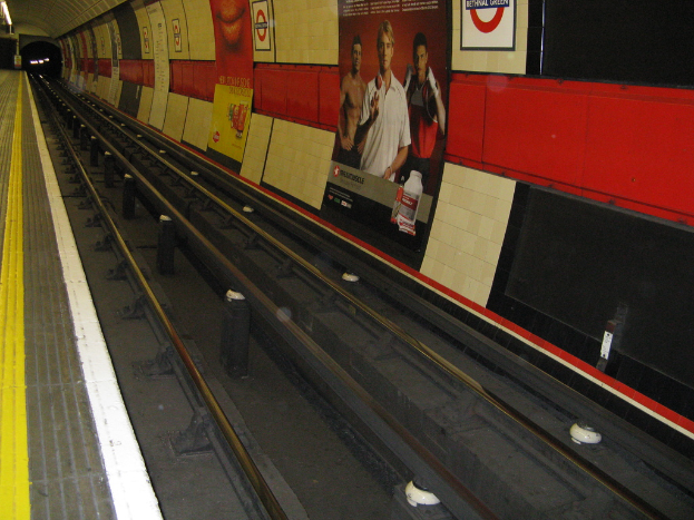 A train track with posters on the adjacent wall.
