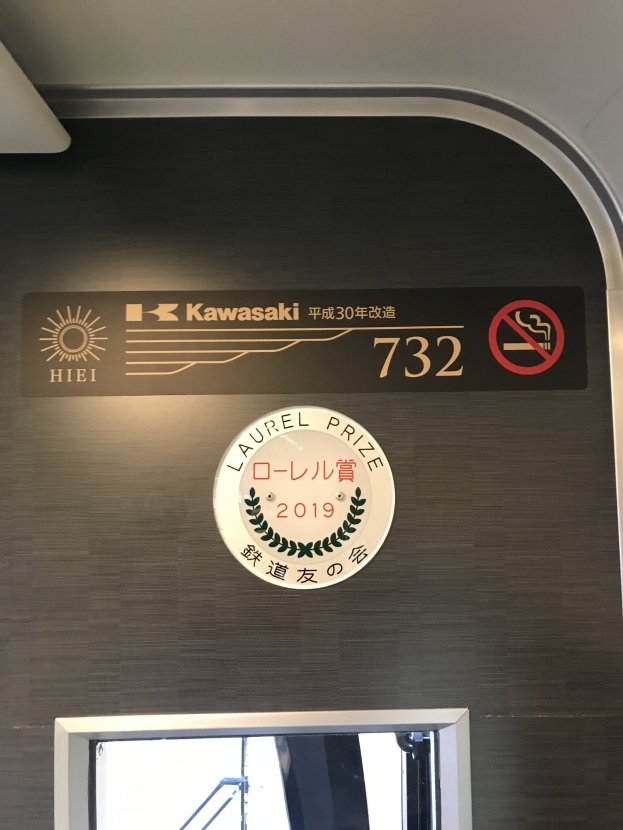 Wand mit einem Schild, auf dem "Kawasaki 732" steht, und einem Glasfenster auf der rechten Seite.