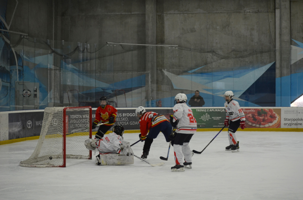 Gruppe von Menschen, die Eis-hoc-key auf einem Eisstadion spielen, mit Helmen und Hockeyschläger, mit einem Tor auf der linken Seite und Bannern im Hintergrund.