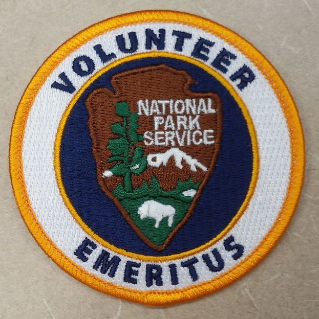 Runder Patch mit blauem Rand und weißem Hintergrund, der den schwarzen Text "Volunteer National Park Service Emeritus" in der Mitte eines gelben Kreises zeigt.