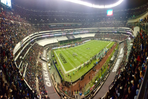 Ein großes Stadion voller Zuschauer, die ein Fußballspiel sehen, mit Spielern und Gegenständen auf dem Feld, beleuchteten Tafeln, Geländern, Bildschirmen und Deckenleuchten.