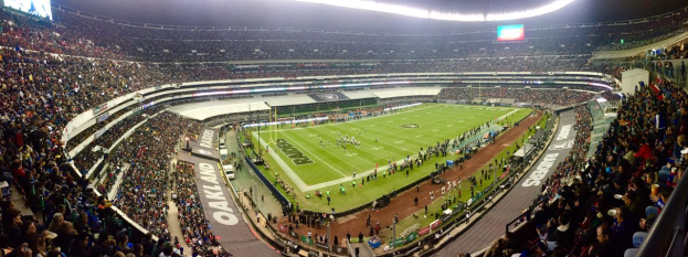 Ein großes Stadion voller Zuschauer, die ein Fußballspiel sehen, mit Spielern und Gegenständen auf dem Feld, beleuchteten Tafeln, Geländern, Bildschirmen und Deckenleuchten.
