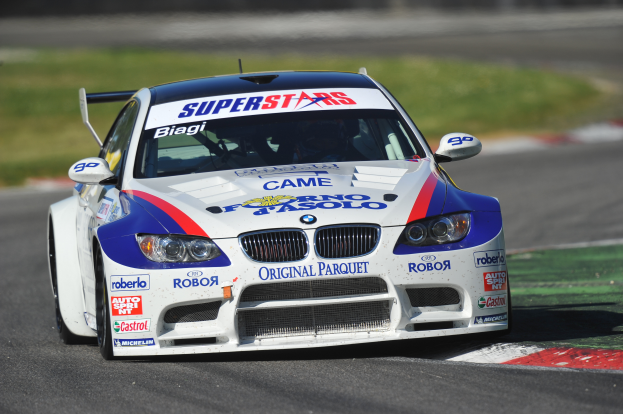 Ein BMW M3 GT3 Rennwagen fährt auf einer Rennstrecke mit Text auf dem Auto und einem unscharfen grünen Hintergrund.