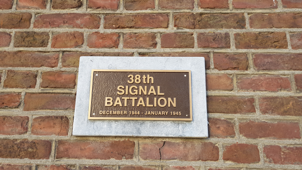 Eine Ziegelwand mit einer rechteckigen Plakette, auf der in fetter, weißer Schrift "38. Signal Battalion" steht.