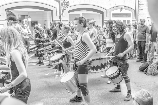 Eine Gruppe von Menschen, die vor einer Stadt stehen und Musikinstrumente spielen, mit einer geschlossenen Glastür und einem Licht im Hintergrund.