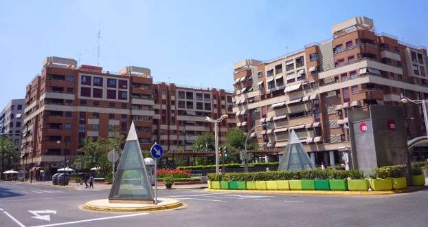 Eine Stadtstraße mit einem zentralen Denkmal, hohen Gebäuden, Straßenmöblierung, Grünanlagen, Fußgängern und einem klaren blauen Himmel.