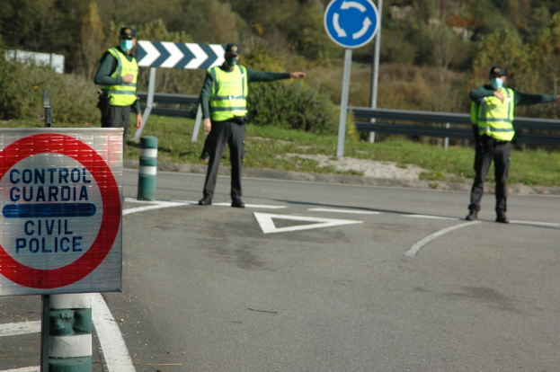 Drei Polizisten in grünen Jacken, schwarzen Hosen und schwarzen Schuhen stehen an der Straße mit einem Verkehrsschild und einem Schuh im Vordergrund und Bäumen, Pflanzen, Gras und einem Geländer im Hintergrund.