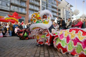 Eine Löwen-Tanzvorstellung während eines chinesischen Neujahrsfestes in Amsterdam mit einer Zuschauermenge und städtischen Gebäuden im Hintergrund.