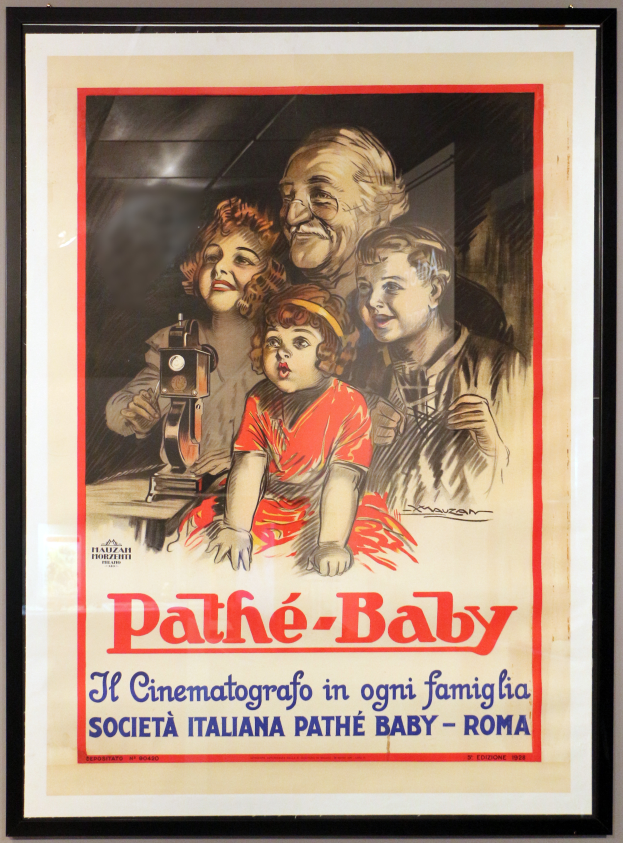 Ein Foto Rahmen an der Wand zeigt ein Plakat einer Familie mit dem Text "Pathé-Baby - Il Cinematografico in Ogni Famiglia Società Italiana Pathé Baby - Roma."