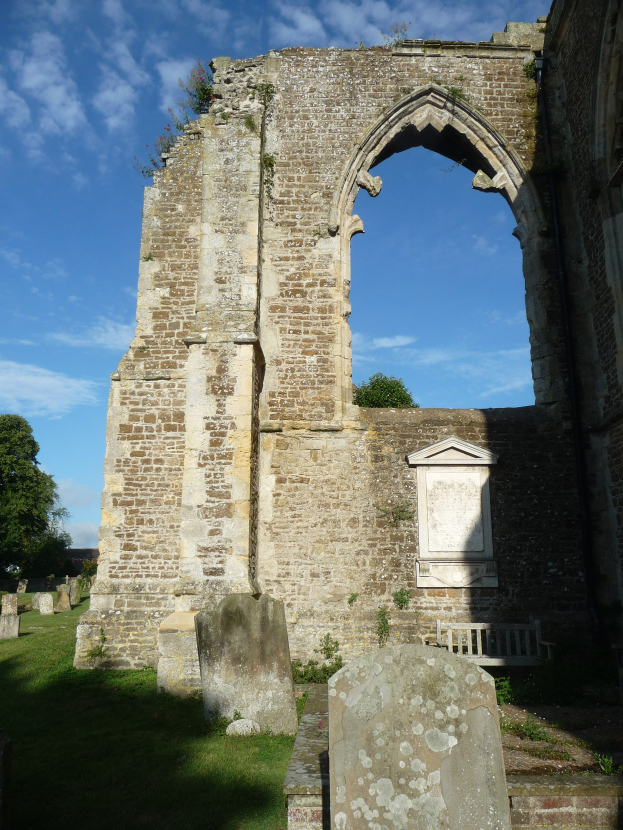 Die Ruinen der St. Mary's Church in St. Margaret's, Suffolk, England, mit einem von Gras umgebenen Bogen, Grabsteinen, Bäumen und einem bewölkten Himmel.