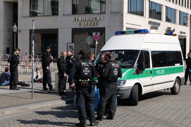 Polizeibeamte vor einem Starbucks-Café mit einem Van rechts und Menschen links, mit einem Gebäude, Schild, Laterne und Zaun im Hintergrund.