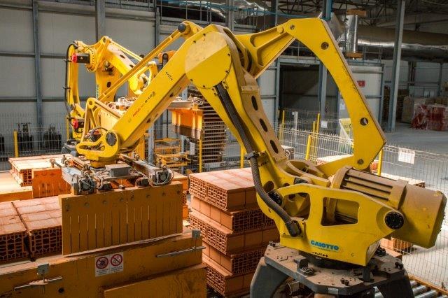 Großes Industriegebäude mit gestapelten Kisten, Überhead-Kränen, Zaun, Pfählen und einer fernen Wand in einer Fertigungsumgebung.