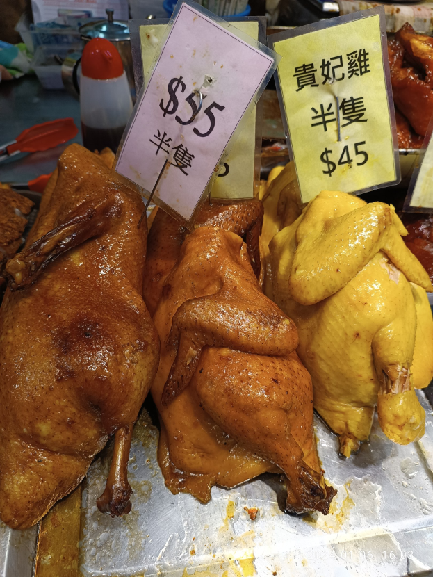 Eine Gruppe von Hühnern auf einem Metalltablett mit Preisschildern vor dem Hintergrund verschiedener Marktartikel.