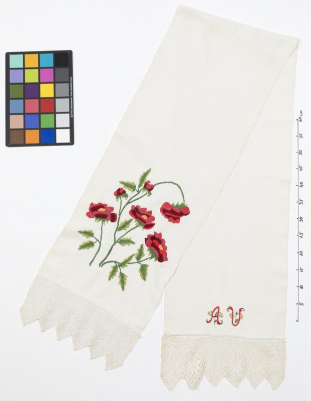 Weißes Taschentuch mit roten Rosen, das neben einer Waage und einer Farbpalette liegt.