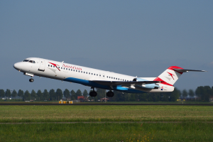 Austrian Airlines Embraer ERJ-190 Flugzeug beim Abheben vom Frankfurter Flughafen, mit grünem Gras darunter und Bäumen und Gebäuden im Hintergrund unter einem sichtbaren Himmel.