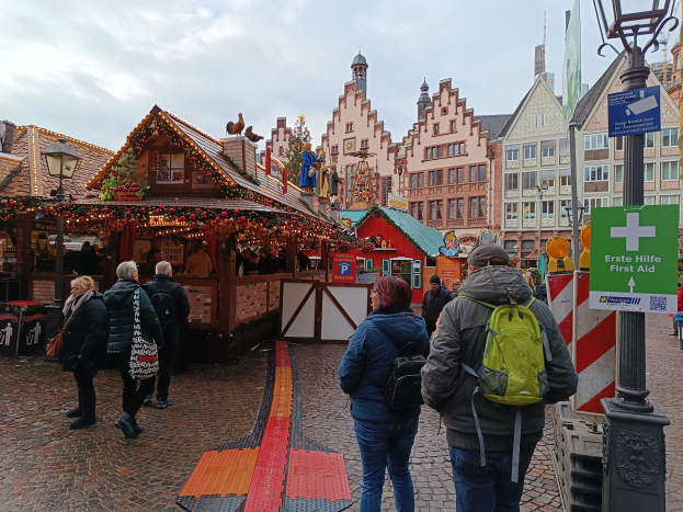 Menschen auf Kopfsteinpflasterstraße neben einem Weihnachtsmarkt in Nürnberg, Deutschland, mit Laternen und Infotafeln im Blickfeld.