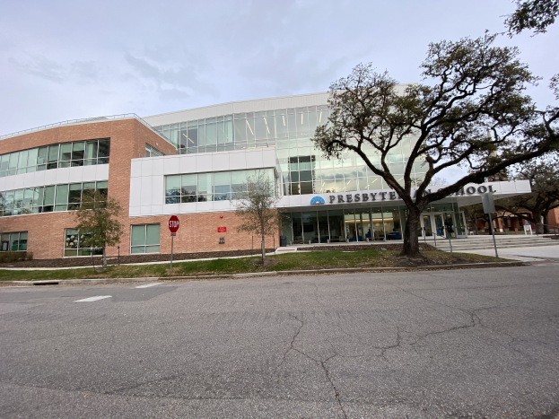 Presbyte Mittelschule, ein großes Gebäude mit vielen Fenstern, umgeben von Bäumen, Gras, Schildern, Pfählen und einer Straße, mit einem bewölkten Himmel im Hintergrund.