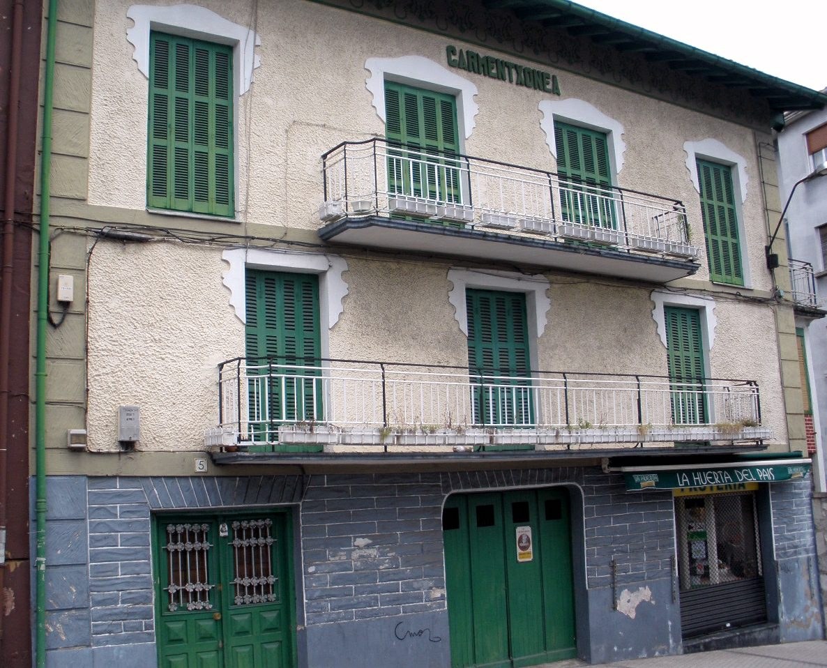 Alter Bau mit grünen Fensterläden, Fenstern, Türen, Geländern und Rohren, neben einer Straße unter dem Himmel.