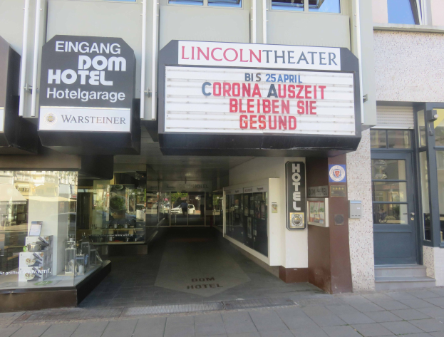 Außenansicht des Lincoln Theaters in Berlin, Deutschland, mit Glasfenstern und -türen und einer Tafel sowie einem Inneren, das eine belebte Stadtlandschaft suggeriert.